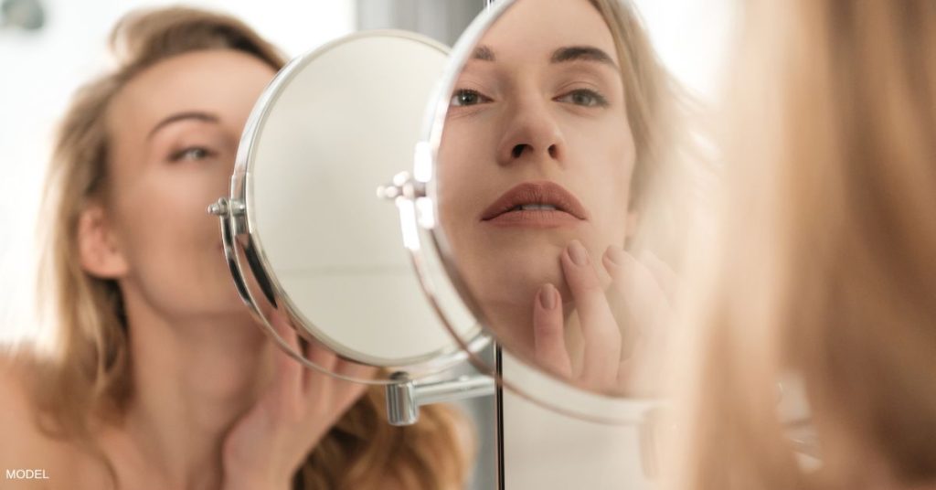 A woman looking at her skin in the mirror (model)